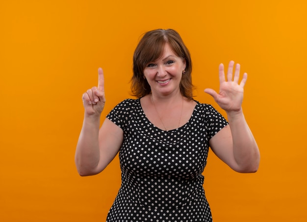 Sonriente mujer de mediana edad mostrando uno y cinco en la pared naranja aislada