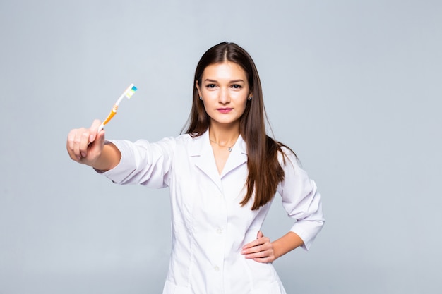 Sonriente mujer médico con frenillos con grandes dientes con cepillo de dientes, aislado en la pared blanca