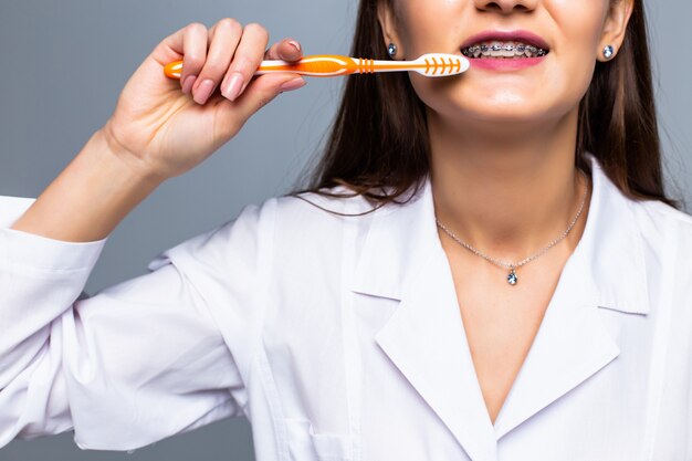 Sonriente mujer médico con frenillos con grandes dientes con cepillo de dientes, aislado en la pared blanca