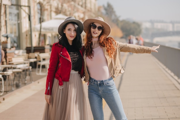 Sonriente mujer morena en falda vintage caminando por la ciudad con su hermana