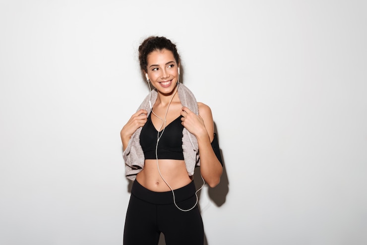 Foto gratuito sonriente mujer morena fitness rizada con toalla escuchando música