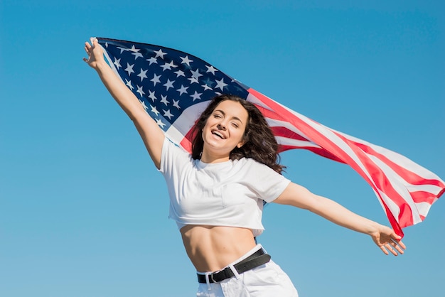 Sonriente mujer morena en ropa blanca con gran bandera de Estados Unidos