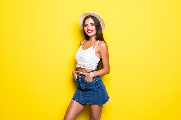 Sonriente mujer morena en suéter posando con los brazos cruzados sobre la pared amarilla