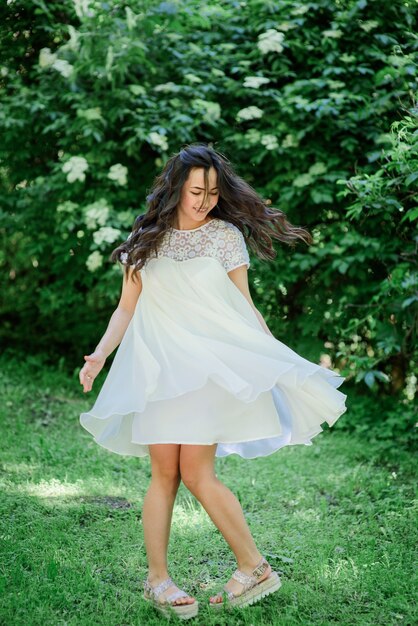 Sonriente mujer morena en vestido blanco plantea en el jardín