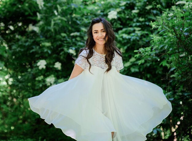 Sonriente mujer morena en vestido blanco plantea en el jardín