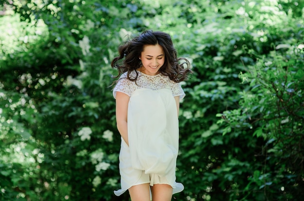 Sonriente mujer morena en vestido blanco plantea en el jardín