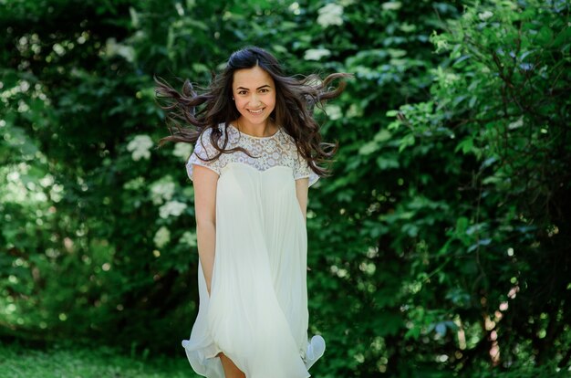 Sonriente mujer morena en vestido blanco plantea en el jardín