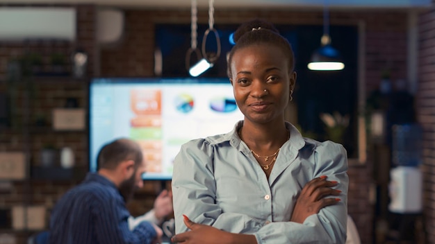 Foto gratuita sonriente mujer de negocios afroamericana cruzando las manos, mirando a la cámara, de pie en el retrato de la puerta de la sala de juntas. gerente de proyecto, empleado de la empresa en espacio de coworking por la noche. disparo de mano.