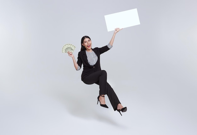 Sonriente mujer de negocios asiática confiada sosteniendo billetes de dinero y pancartas en blanco flotando en el aire