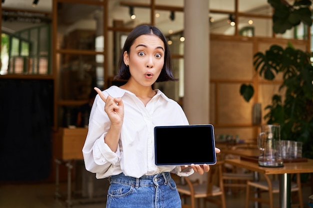 Sonriente mujer de negocios asiática demostrando mostrar la pantalla de la tableta y apuntando a la publicidad de pancartas