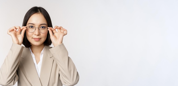 Sonriente mujer de negocios asiática probando nuevas gafas con gafas de pie en traje sobre fondo blanco.