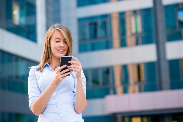 Sonriente mujer de negocios a escuchar la llamada en el teléfono inteligente en frente de su oficina