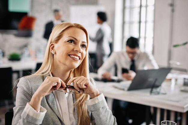 Sonriente mujer de negocios pensativa soñando mientras está en el trabajo Hay gente en el fondo