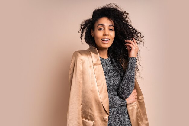 Sonriente mujer negra con chaqueta de seda dorada y vestido brillante con cuerpo bronceado perfecto posando.