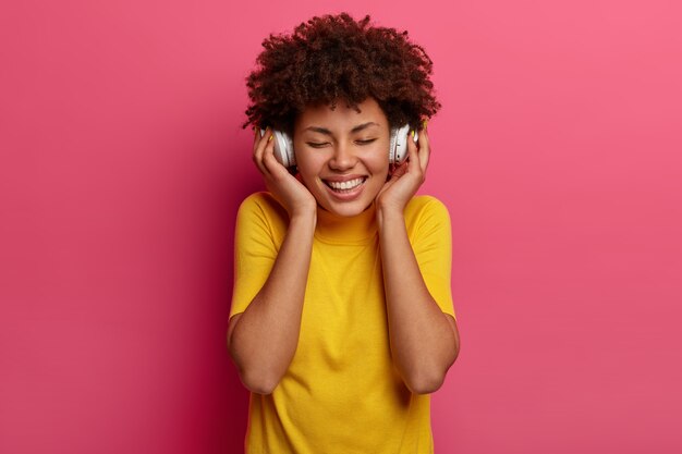 Sonriente mujer de piel oscura disfruta de la melodía, toca los auriculares