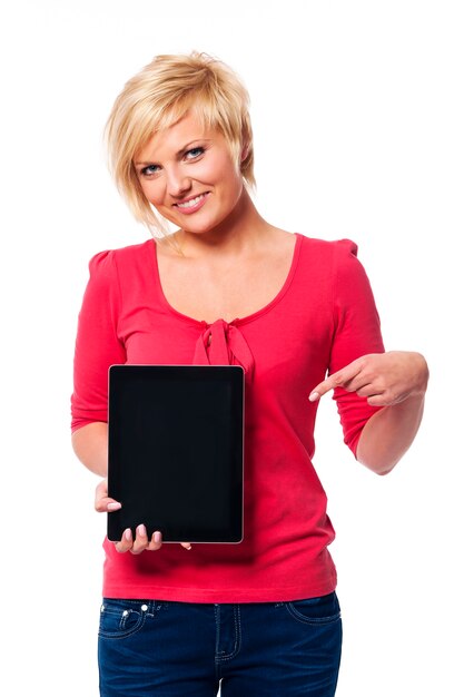 Sonriente mujer rubia apuntando a la pantalla de la tableta digital