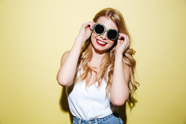 Sonriente mujer rubia feliz con gafas de sol y posando