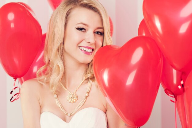 Sonriente mujer rubia con globos rojos en forma de corazón