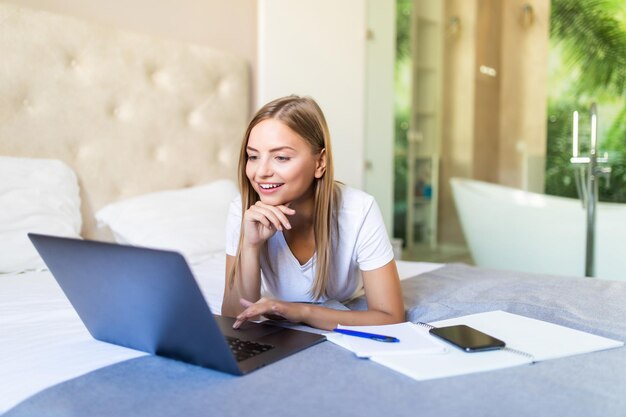 Sonriente mujer rubia con portátil en casa en dormitorio