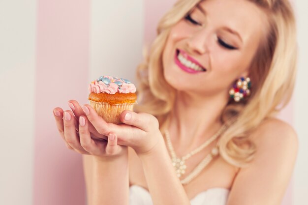 Sonriente mujer rubia sosteniendo pequeño muffin