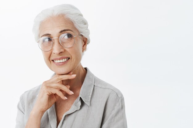 Sonriente mujer senior hermosa en gafas mirando en la esquina superior derecha de ensueño