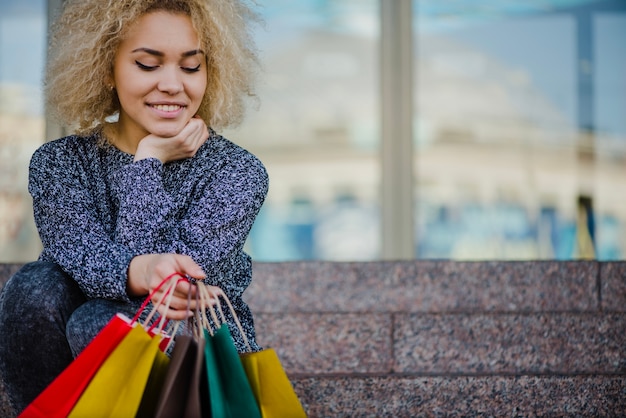 Foto gratuita sonriente mujer sentada con bolsas de papel de colores