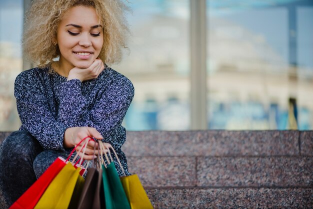 Sonriente mujer sentada con bolsas de papel de colores