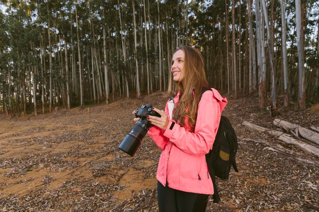 Sonriente mujer sosteniendo la cámara en el bosque