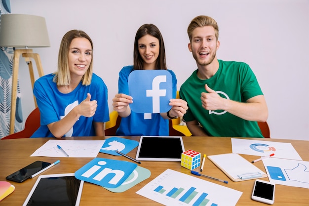 Sonriente mujer sosteniendo el logo de facebook con sus amigos mostrando signo thumbup