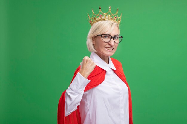 Sonriente mujer de superhéroe rubia de mediana edad en capa roja con gafas y corona