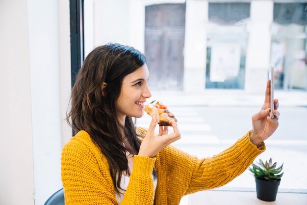 Sonriente mujer tomando selfie y sosteniendo la comida