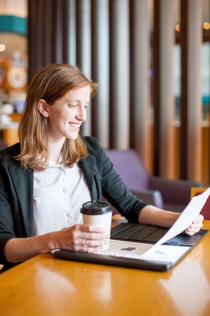 Sonriente mujer trabajando y bebiendo café en el café