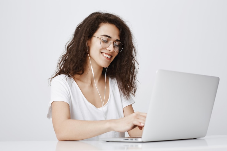 Foto gratuito sonriente a niña bonita que trabaja con la computadora portátil y escucha música con auriculares