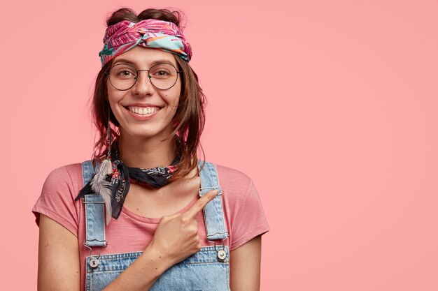 Foto gratuita sonriente niña hippie con expresión feliz, muestra la dirección al extraño