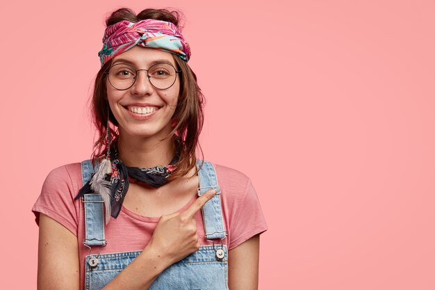 Sonriente niña hippie con expresión feliz, muestra la dirección al extraño