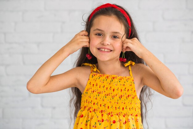 Sonriente niña linda con cerezas cerca de la oreja como pendientes