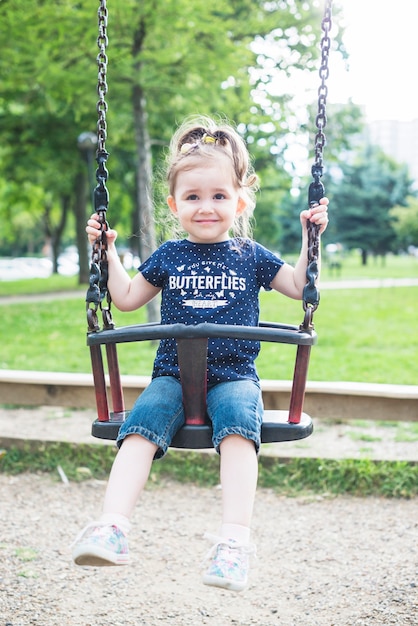 Sonriente niña linda sentada en columpio en el parque