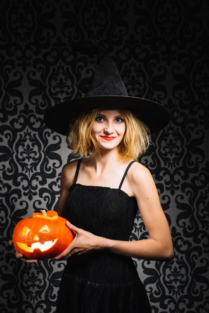 Sonriente niña en sombrero de bruja con calabaza