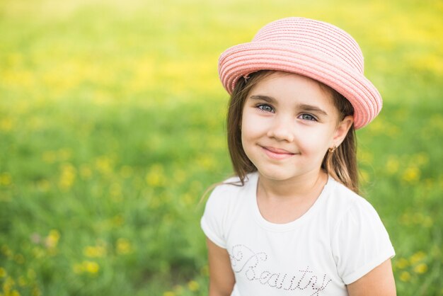 Sonriente niña con sombrero rosa en la cabeza en el parque