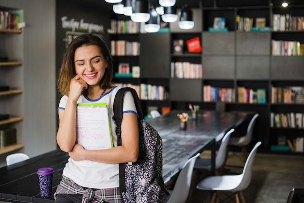 Sonriente niña sosteniendo cuadernos apoyándose en la mesa