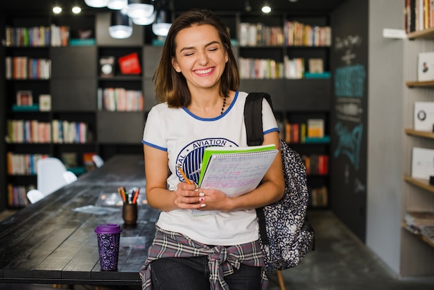 Sonriente niña sosteniendo cuadernos apoyándose en la mesa