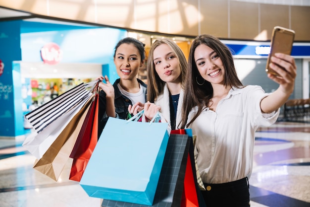 Sonriente niñas tomando selfie con bolsas de papel