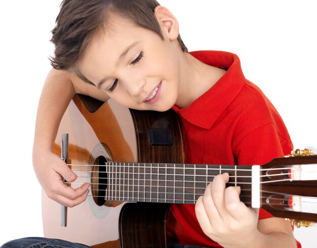 Sonriente niño caucásico está tocando la guitarra acústica - aislada sobre fondo blanco