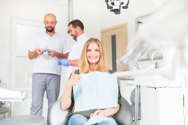 Sonriente paciente femenino gesticular signo bien en frente de dos dentistas hombres