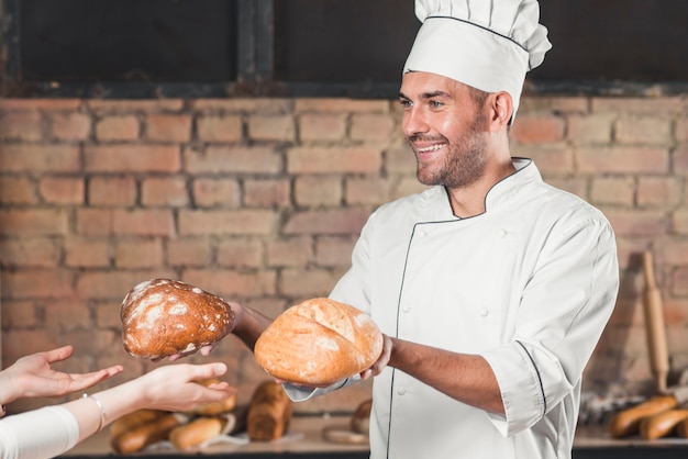 Foto gratuita sonriente panadero macho dando dos pan bollo a cliente femenino
