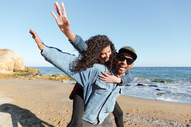 Sonriente pareja amorosa africana caminando al aire libre en la playa