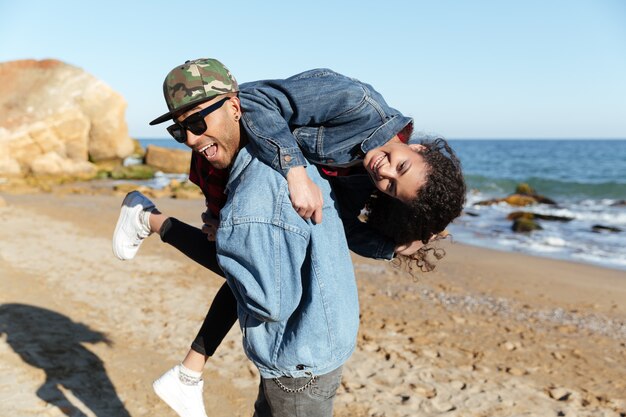 Sonriente pareja amorosa africana caminando al aire libre en la playa