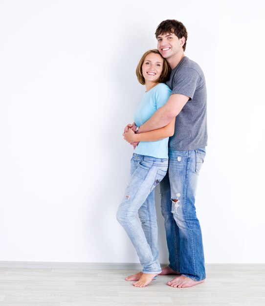 Sonriente pareja amorosa feliz en casuals de pie en la habitación vacía - en el interior