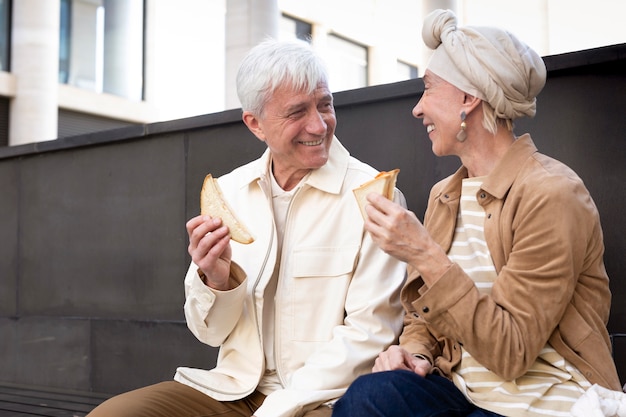 Sonriente pareja de ancianos al aire libre disfrutando de un sándwich juntos