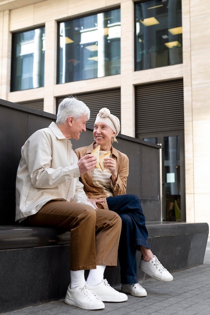 Sonriente pareja de ancianos al aire libre disfrutando de un sándwich juntos